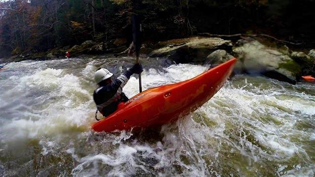 A kayaker in a red boat paddles through whitewater on Slippery Rock Creek